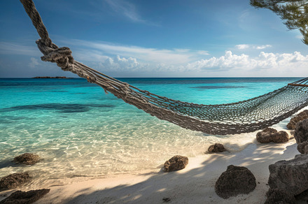 A hammock hanging between two trees on a tropical beach with cle