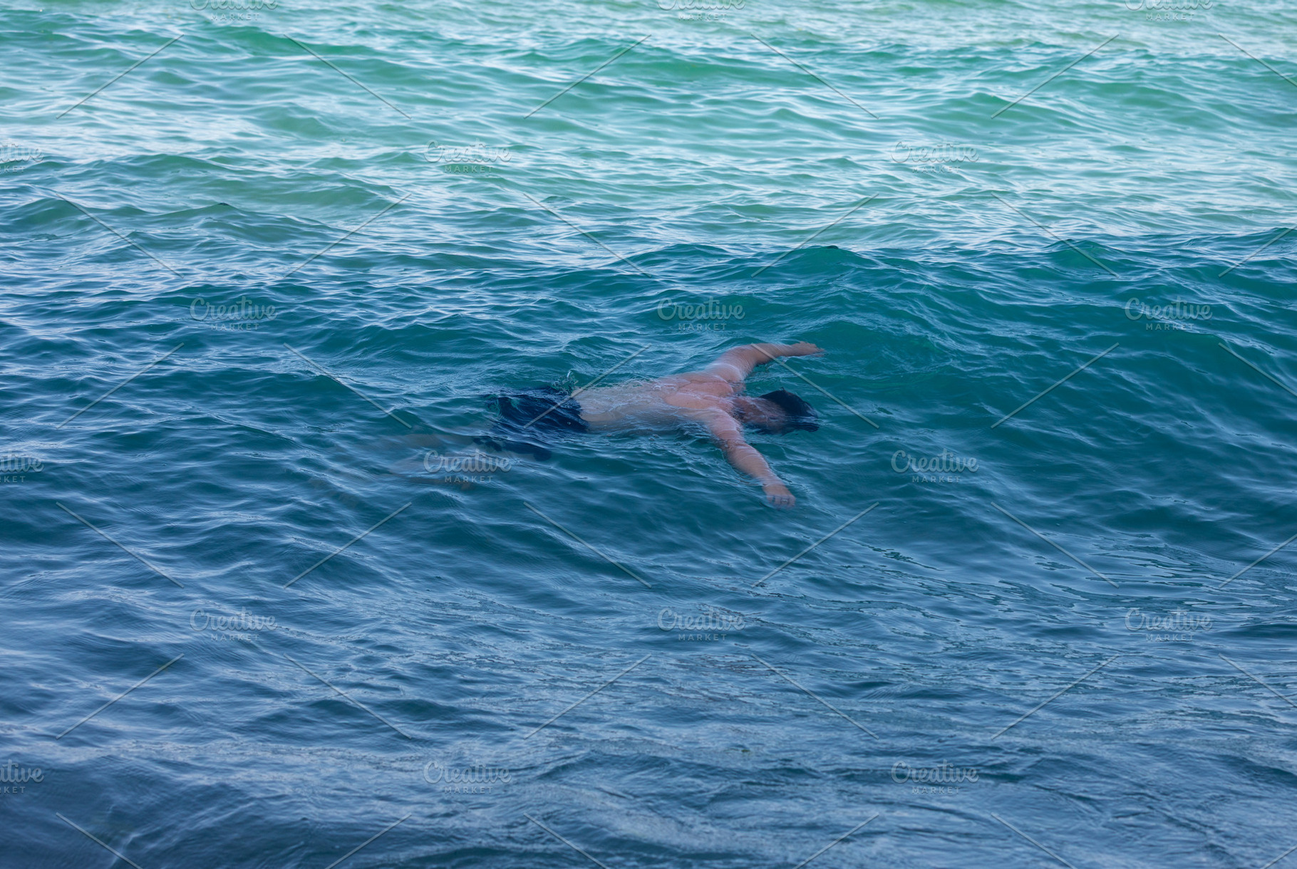 Male swimmer in blue water, captured mid-stroke, surrounded by rolling ocean wa, a Person Photo by Ales Munt