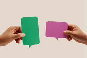 Two hands hold colorful blank speech bubbles over a neutral back, a Photo by salmon.black