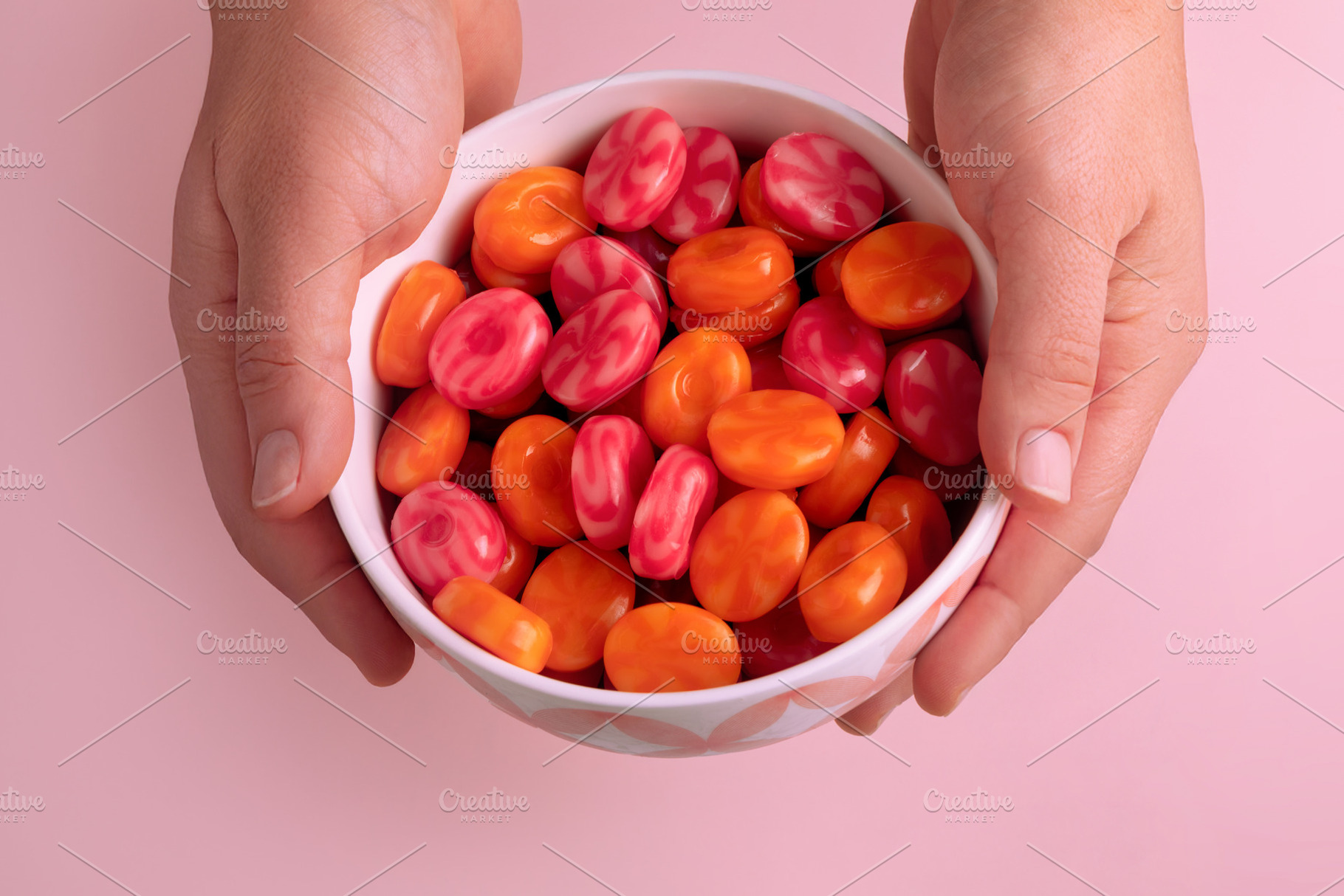 Bowl of vibrant orange and pink candies held in two hands on a p, a Food & Drink Photo by Ales Munt