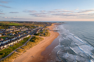 Coastal town houses lining a vast sandy beach at sunset, with wa, a Photo by Studio ANNA