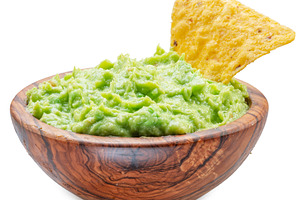 Guacamole bowl and corn chips dipped in it on white background., a Food & Drink Photo by Volff