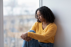 Unhappy young black woman looking out window, having depressive thoughts at hom, a Photo by Prostock-Studio