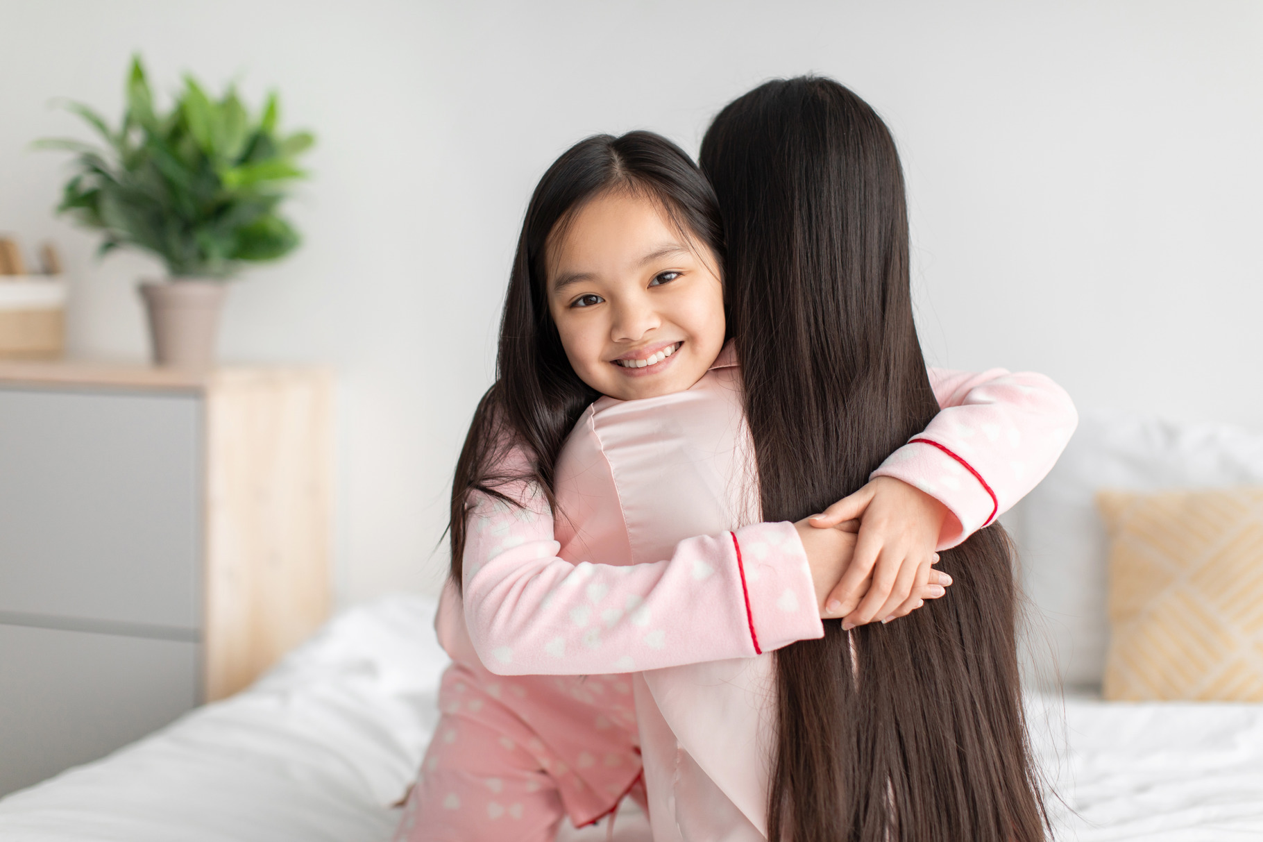 Satisfied happy chinese teenage girl hugging young lady on bed in ...