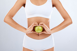 Digestion, apple and woman stomach with hands in heart shape for nutrition, detox diet and studio background. Fruits, wellness and healthy abdomen body with care, love and lose weight for strong gut, a Photo by Peopleimages.com