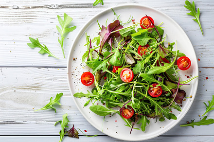 Fresh salad with microgreen, arugula and tomatoes in plate on wooden table, a Food & Drink Photo by AlyaAnd