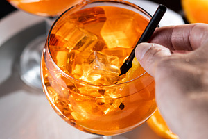 Hand holding Aperol Spritz cocktail with ice and orange slice, a Food & Drink Photo by etorres69