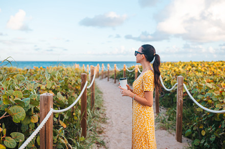 Young happy woman walking on the beach with coffee to go, a Person Photo by travnikovstudio