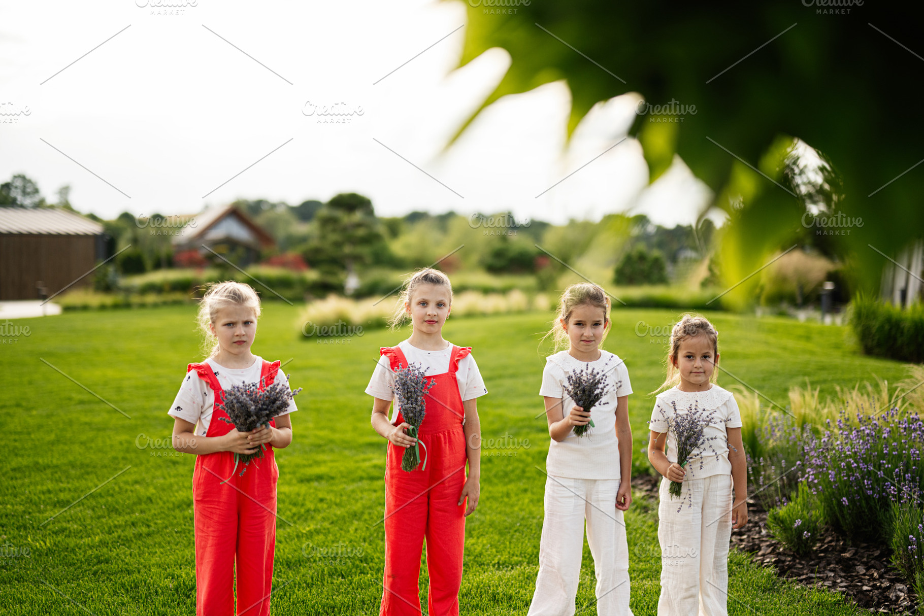 Four young girls holding lavender flowers in a lush outdoor garden setting, a Photo by AS photostudio