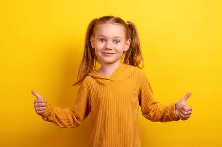 Smiling young girl in a mustard sweater showing two thumbs up ag