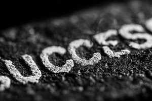 Close-up of success text on textured surface in black and white lighting, a Photo by AS photostudio