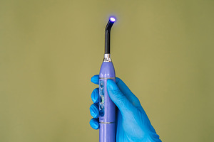 Dental curing light in gloved hand on green background, a Technology Photo by Red Hot Chili Pepper Shop
