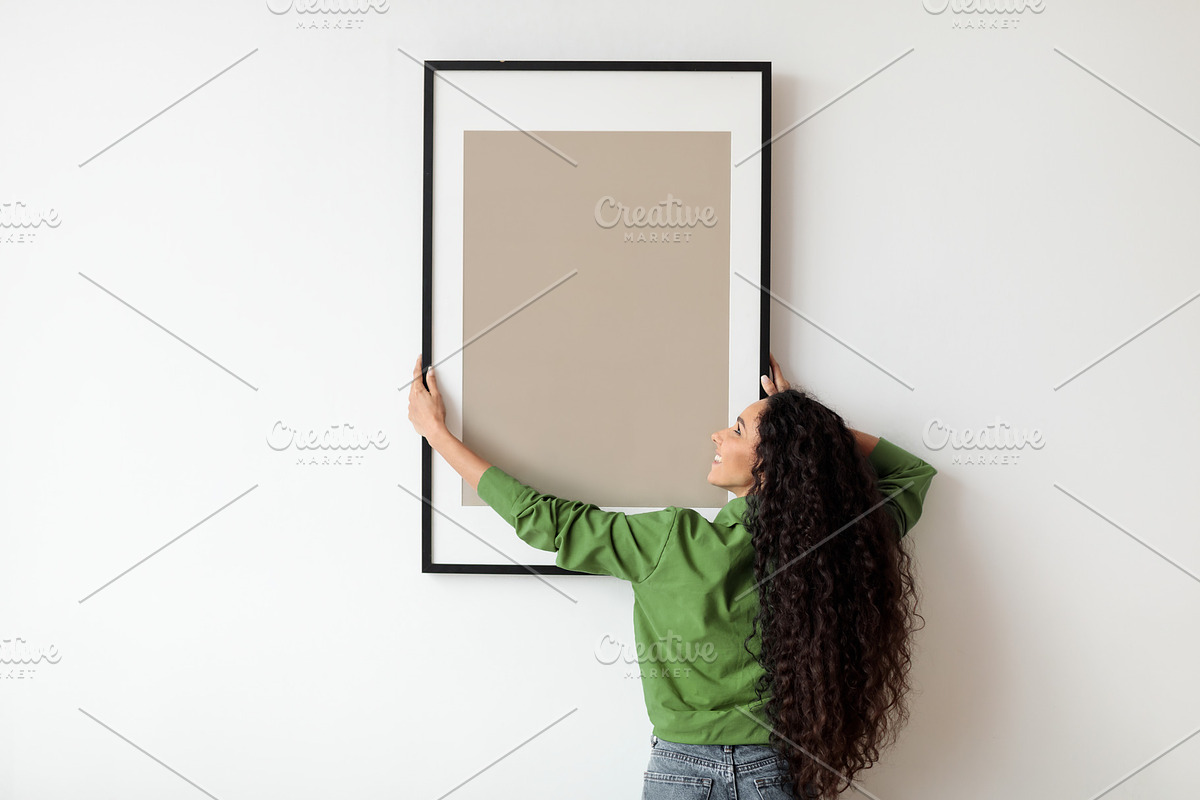 Woman Hanging Frame With Empty Poster On White Wall Indoors, a Photo by Prostock-Studio (Photo 2 of 2)