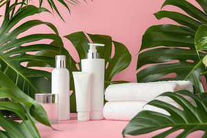 Blank cosmetic containers with towels and green leafs on pink background, a Beauty & Fashion Photo by AlyaAnd