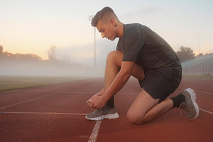 Runner tying shoe on track at foggy morning, a Photo by DanFLCreativo