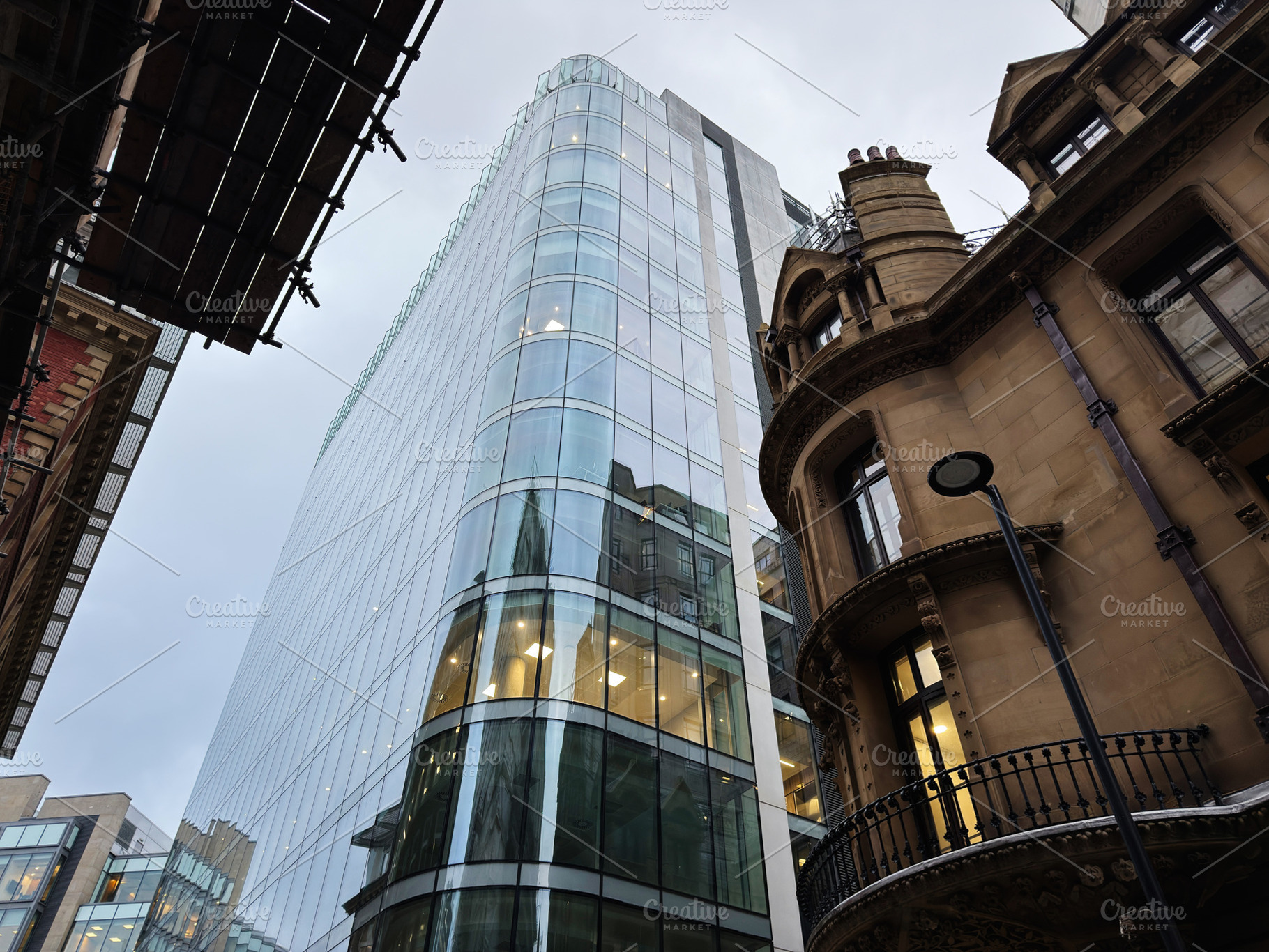 Modern glass skyscraper towers over historic brick building in Manchester city, a Photo by AS photostudio