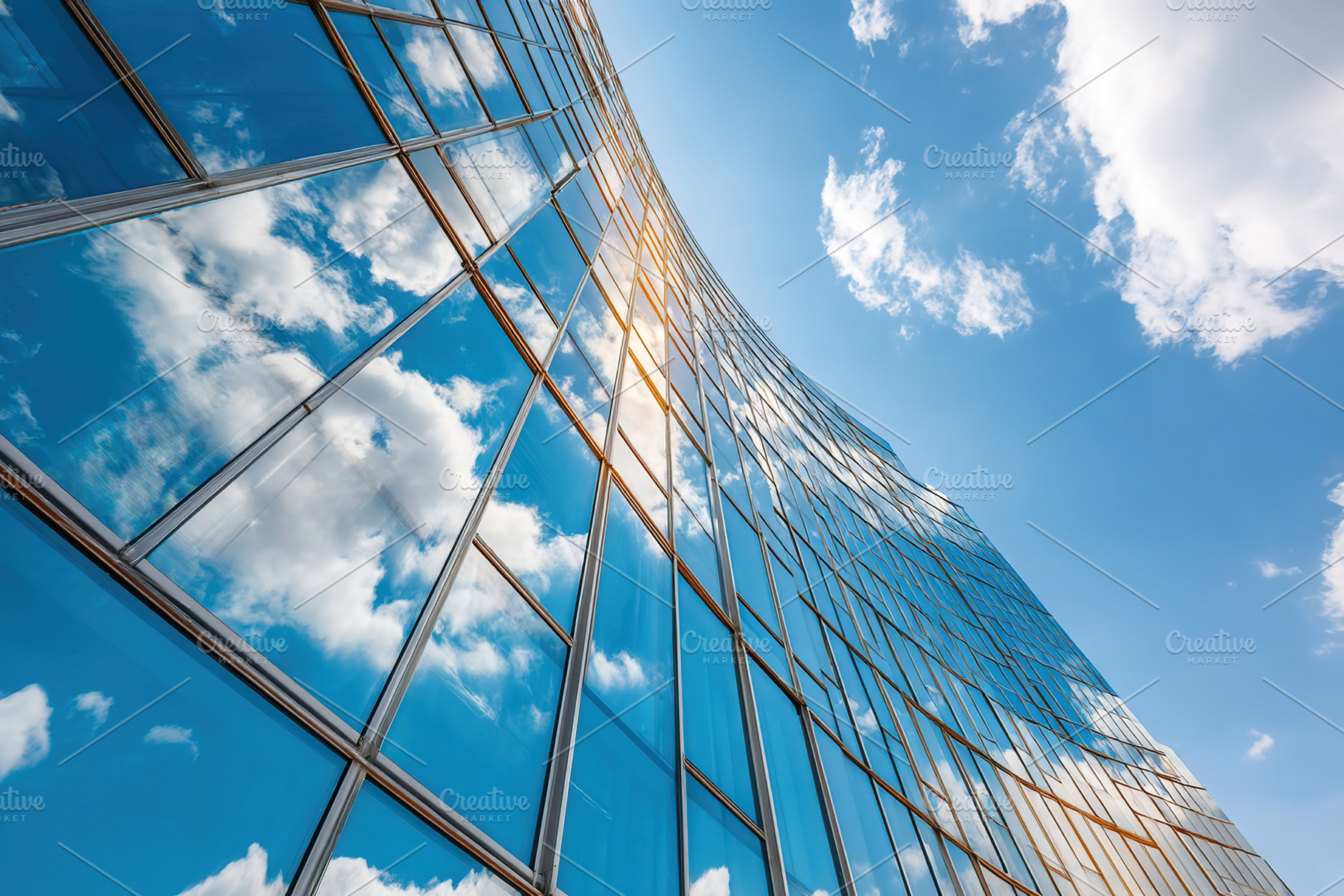 Building facade reflects clouds in clear blue sky during sunny daylight hours, an Architecture Photo by AlyaAnd