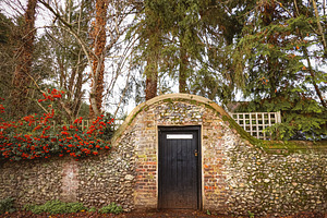 Old weathered stone wall and brick archway enclosing a hidden black wooden door, a Photo by Studio ANNA