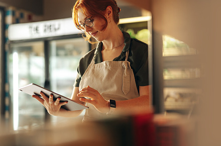 Cheerful store owner using a digital tablet in her grocery store, a Person Photo by Jacob Lund