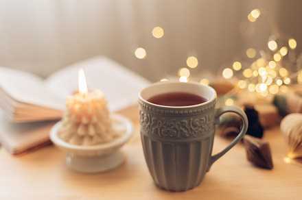 Cozy winter still life. Mug with tea or coffee, burning candle, book, gift box