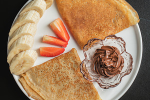 A plate of crepes filled with chocolate spread and topped with b, a Food & Drink Photo by Budarinphoto