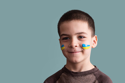 Child against war. Upset Ukrainian boy with bue yellow flag on his face