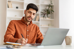 Portrait of focused Arab man using pc and writing, a Photo by Prostock-Studio
