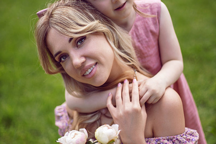 beautiful young mother with a baby daughter in pink dresses sitting on a green, a Person Photo by SaulichPhoto