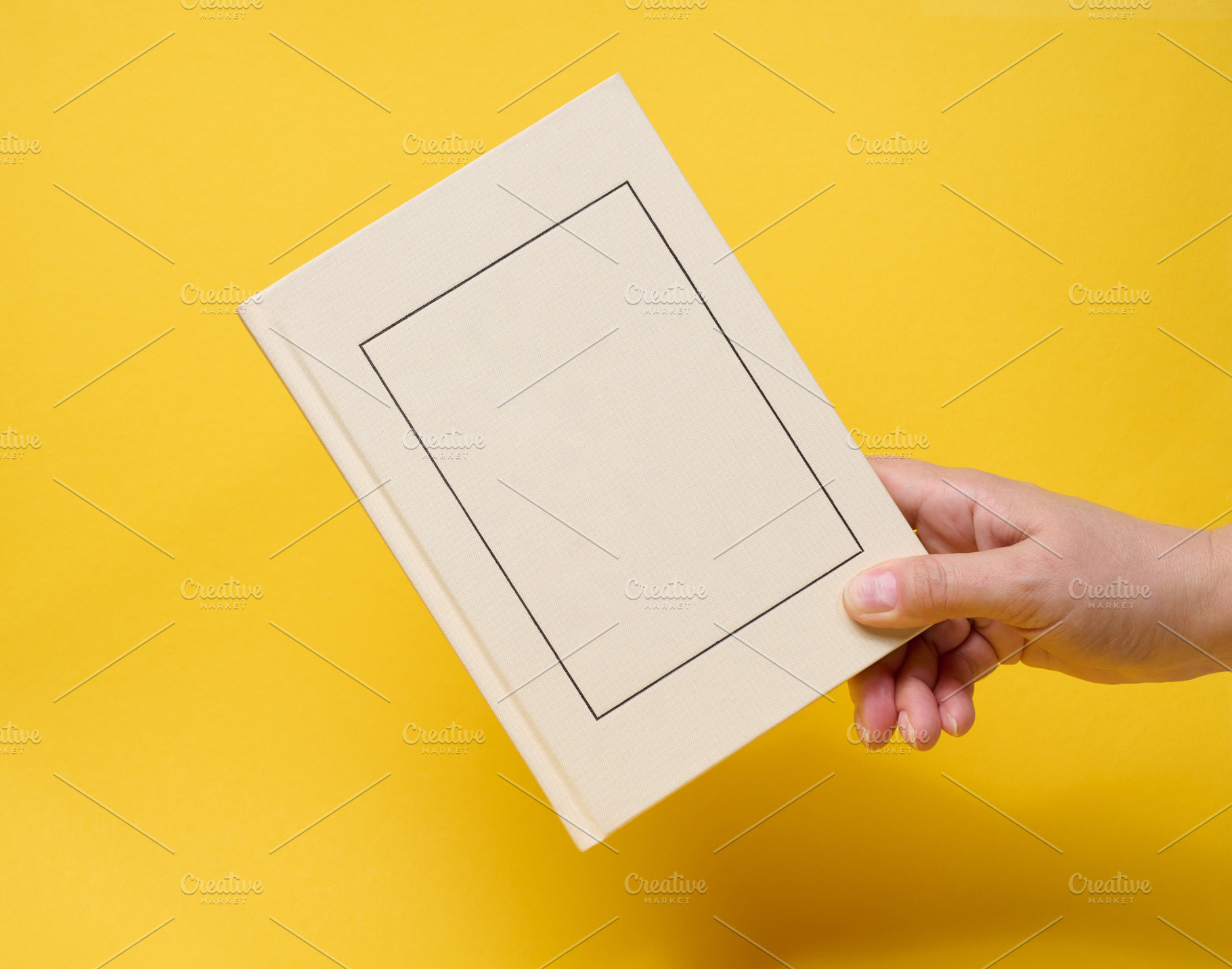 A person holding a closed light hardcover book with a frame on t, a Person Photo by ndanko