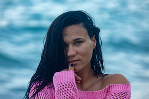 Portrait of a woman with dark hair in a pink sweater standing in front of ocean, a Person Photo by Ales Munt