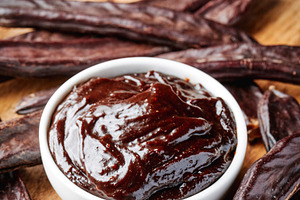 bowl of carob spread and pods on a wooden table, a Photo by Nito