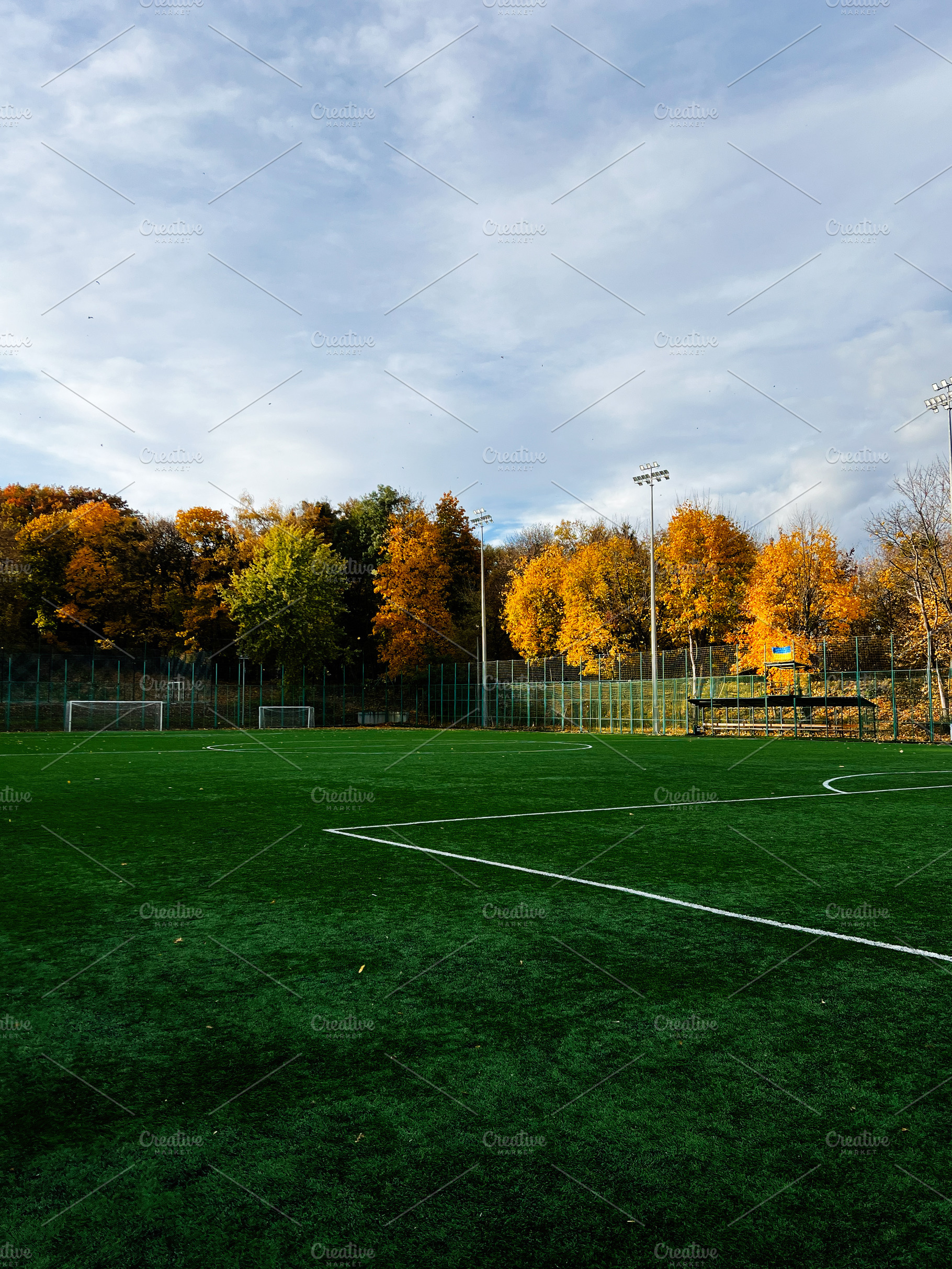 Autumn football field under blue sky with colorful trees and empty pitch, a Photo by AS photostudio