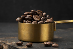 Roasted coffee beans are heaped into a golden metal measuring cu, a Food & Drink Photo by ndanko
