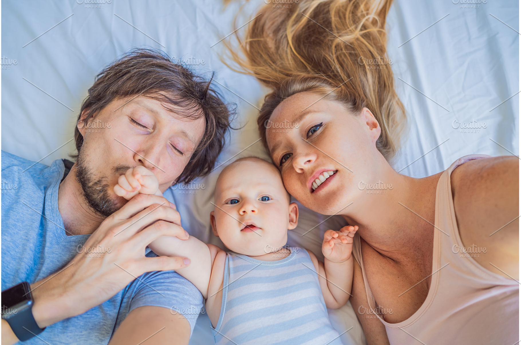 Baby lying with mother and father on, a Person Photo by Elizaveta Galitskaya