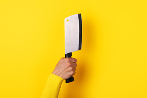 Close-up of a hand gripping a meat cleaver against a vibrant yel, a Food & Drink Photo by Ales Munt