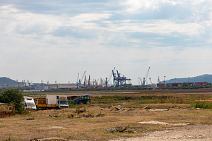 Wide view of an industrial port with cranes and containers, seen from a grassy, an Industrial Photo by Ales Munt
