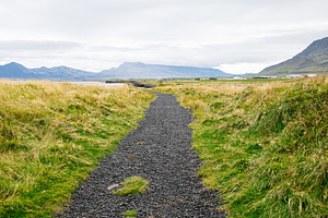 Scenic gravel path in Iceland surrounded by grasslands and mountain views, a Nature Photo by AS photostudio