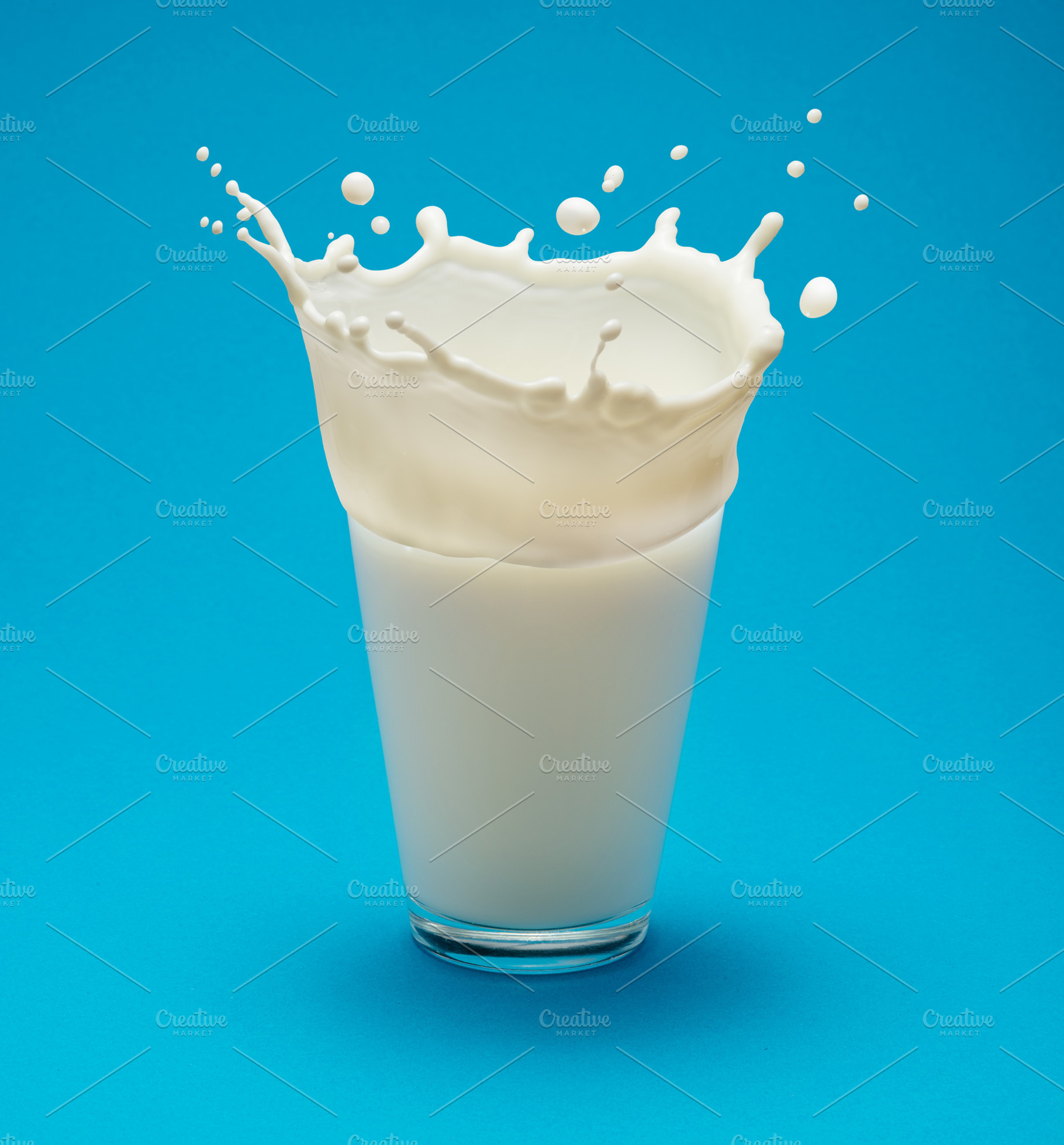 Milk splash (crown) on a glass of milk isolated on blue backgrou, a Food & Drink Photo by Volff