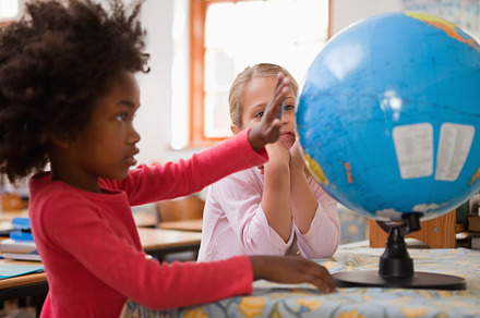 Happy schoolgirls looking at a globe, a Photo by wavebreak