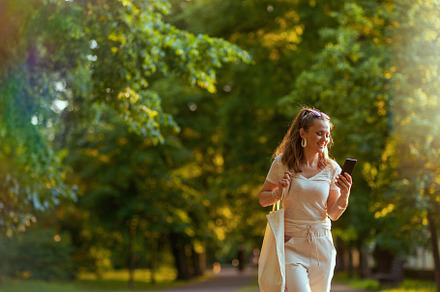smiling stylish woman in shirt using phone and walking, a Person Photo by Alliance Images
