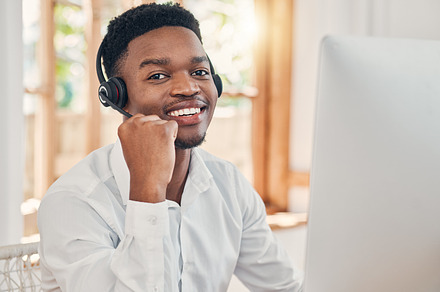 Black man, customer support service with a smile and working for digital call center or online telemarketing business. Crm consultant at office desk, helping caller and consulting computer for fix, a Photo by Peopleimages.com