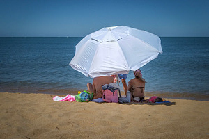 Couple relaxing under an umbrella on a sunny beach, a Person Photo by DanFLCreativo