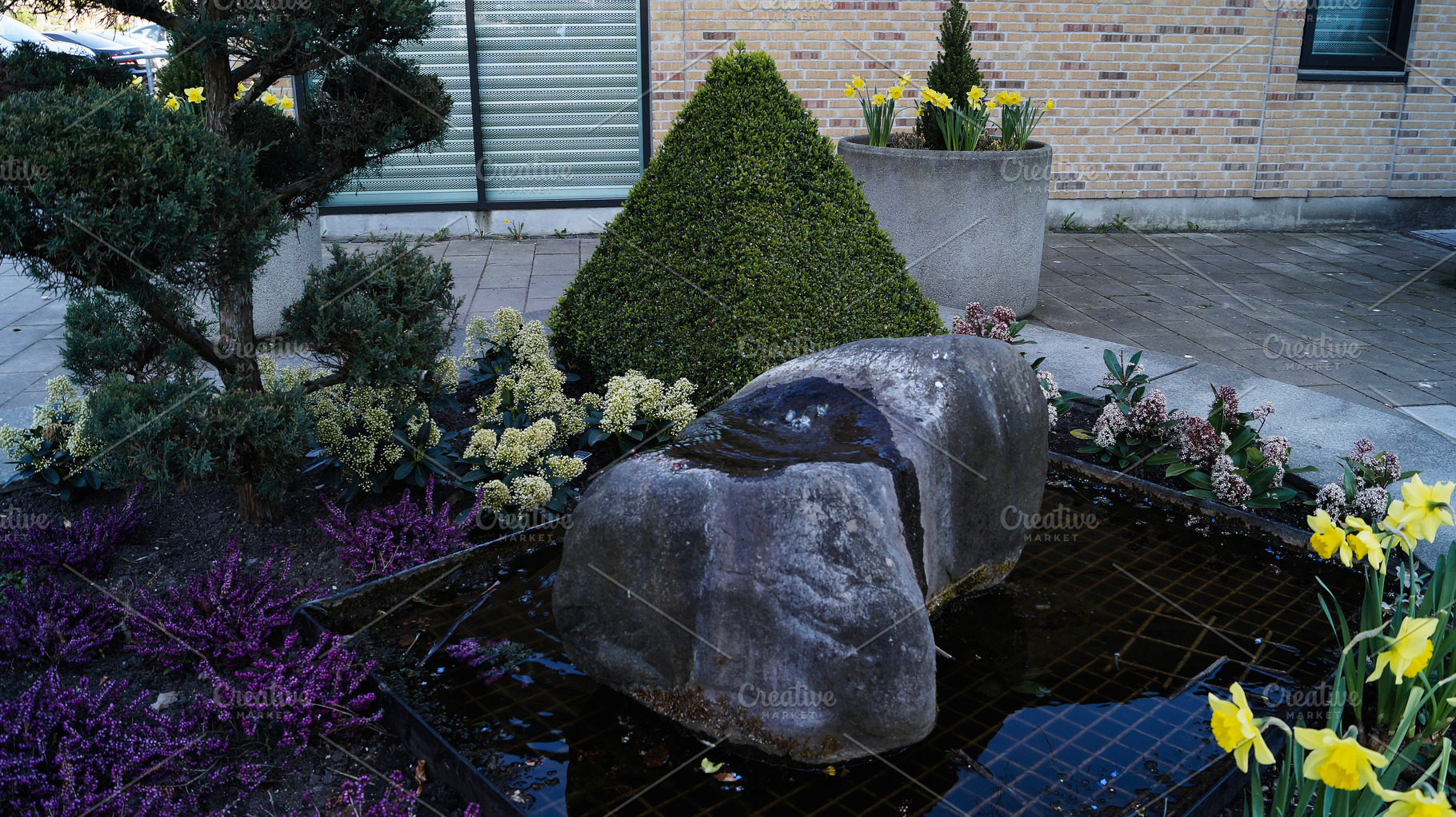 Small landscaped garden with stone fountain features and spring flowers in Denm, a Photo by AS photostudio