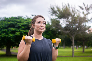 Woman performing dumbbell front raise during outdoor strength workout