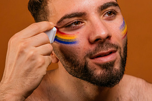 Man applying rainbow face paint for pride celebration, a Photo by karrastock