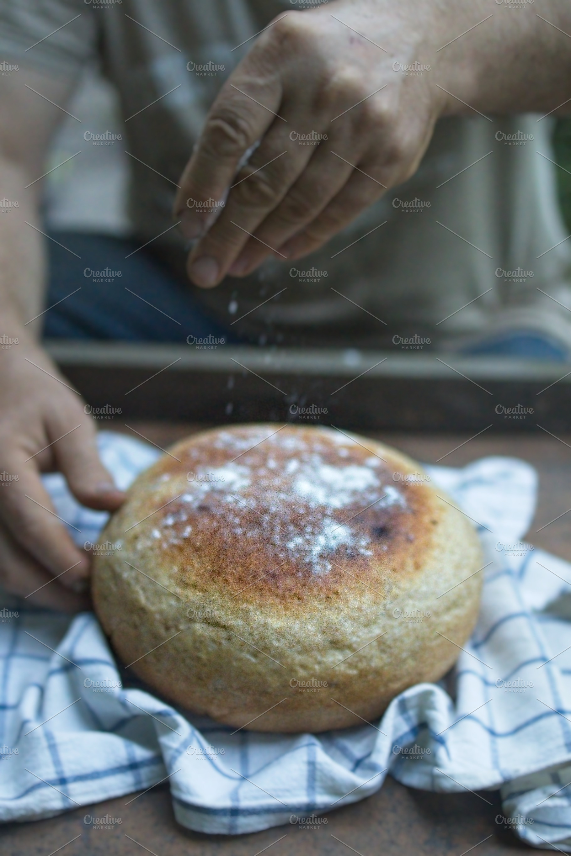 Baker's hand sprinkles flour on fresh bread close-up. A man finishes baking, de, a Food & Drink Photo by TanaCh