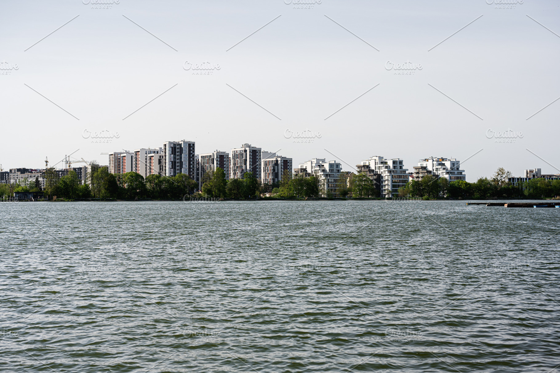 Modern residential buildings along a serene lake under a clear sky, a Photo by AS photostudio