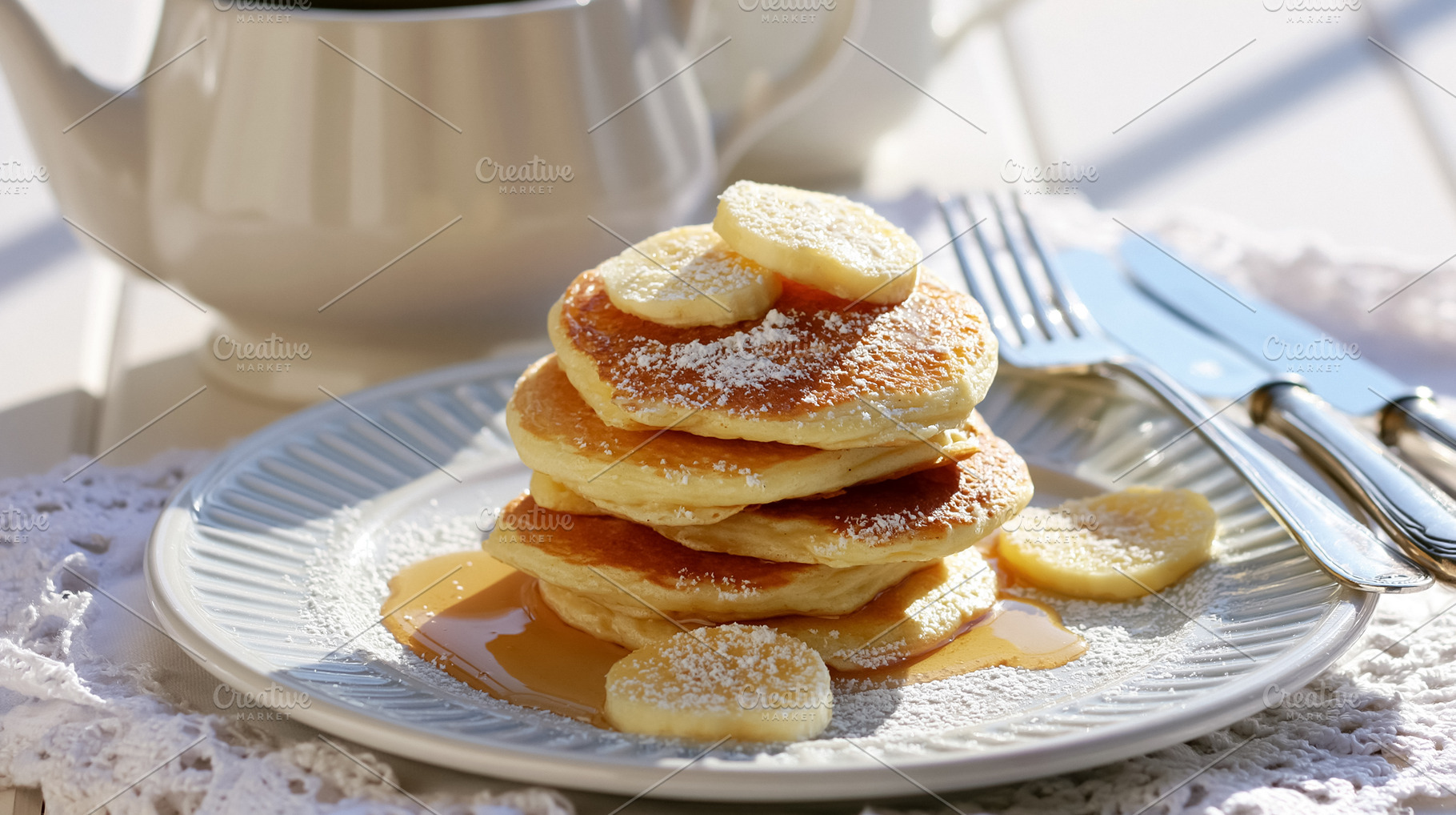 Pancakes stacked on a plate, topped with banana slices, powdered sugar, and map, a Photo by Studio ANNA