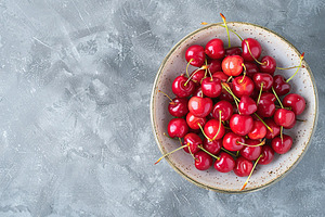 Flat lay of fresh cherries in bowl on grey background, a Food & Drink Photo by AlyaAnd