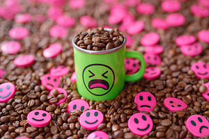 Decorative coffee mug with face design surrounded by coffee beans and smiley to, a Food & Drink Photo by AlyaAnd